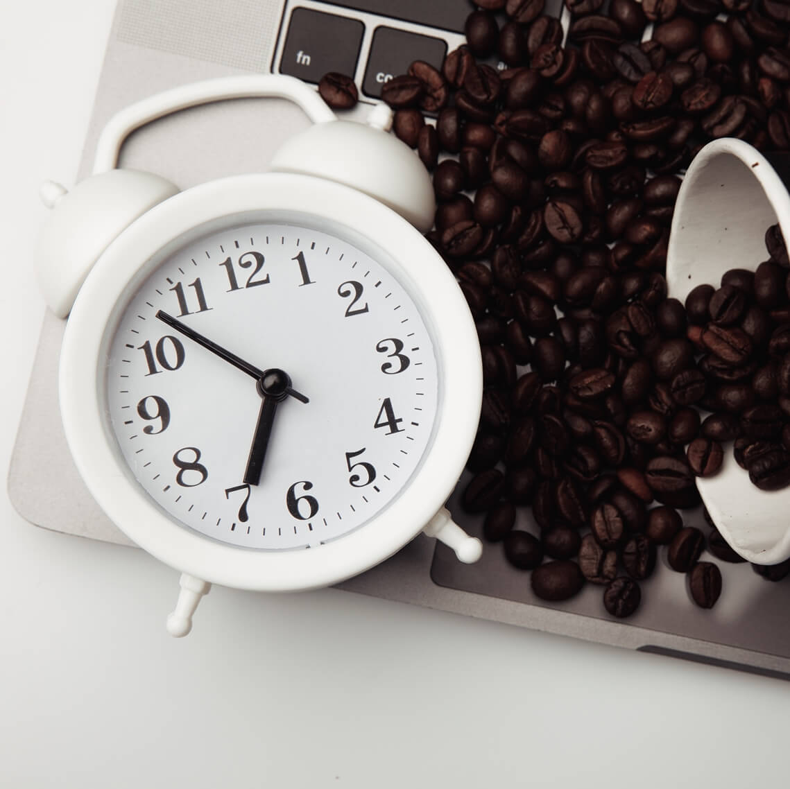 a clock and coffee beans on an opened laptop
