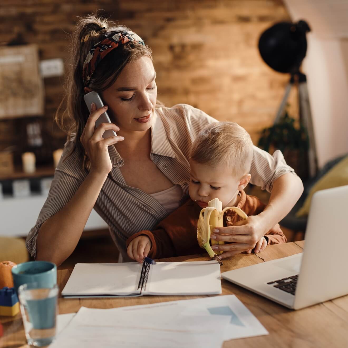 a busy business woman holding a baby and speaking on the phone before a monitor